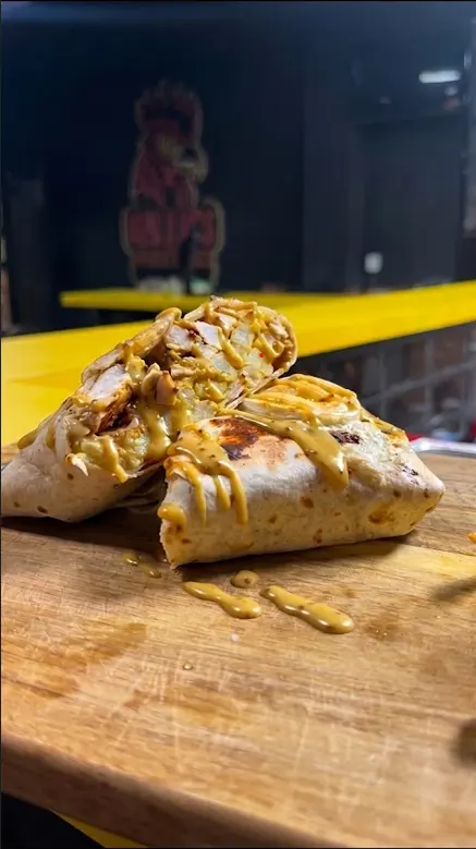 French taco bañado en salsa de queso sobre una tabla de madera, con el rótulo del local al fondo